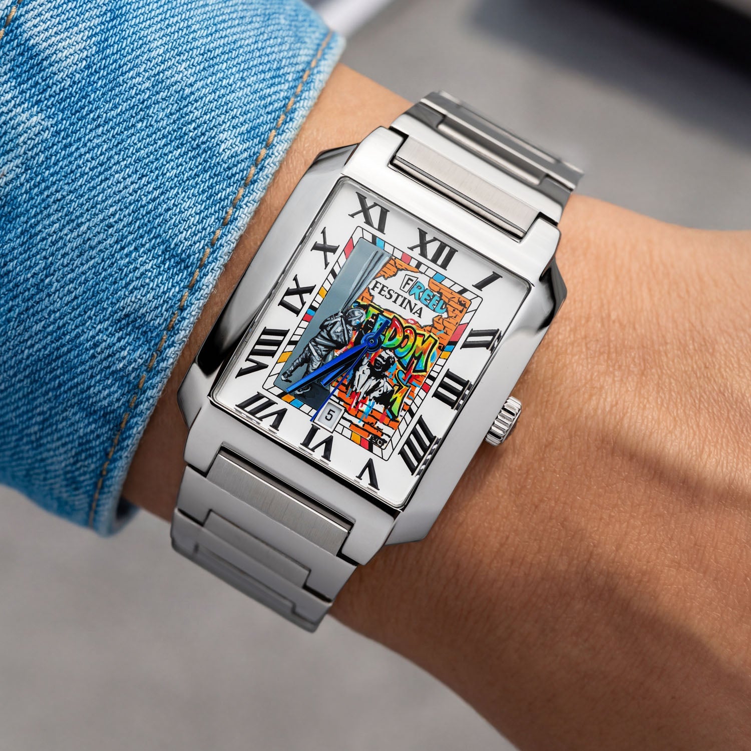 Festina Freedom 36 mm on wrist — hand-painted street-art dial featuring colorful “FREEDOM” graffiti lettering, stencil figures, and orange brick-wall artwork on a rectangular stainless-steel case. Limited edition by IFL Watches.
