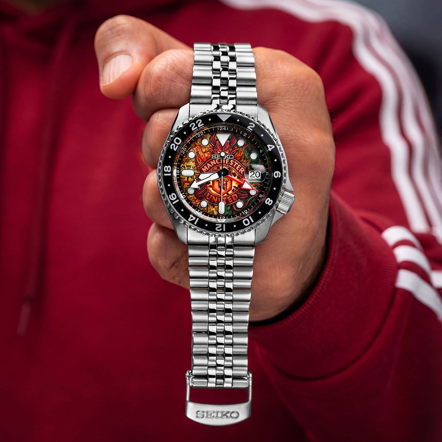 The Red Devils Concept held in hand — full view of the hand-painted football crest dial with red, gold, and green heritage colors on a 42.5mm stainless steel GMT automatic with jubilee bracelet, a bespoke timepiece by IFL Watches.