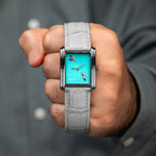 Laphont Bloc Cloudling — Held in a closed fist toward the camera against a grey shirt, the teddy bear and its balloons in full view above the pale grey croc-embossed strap, a hand-painted limited edition timepiece by IFL Watches