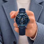 Mandetbrote Wandering Hour Dark Blue — Held in hand against a blue-grey coat, showing the hour discs and central seconds hand, available at IFL Watches.