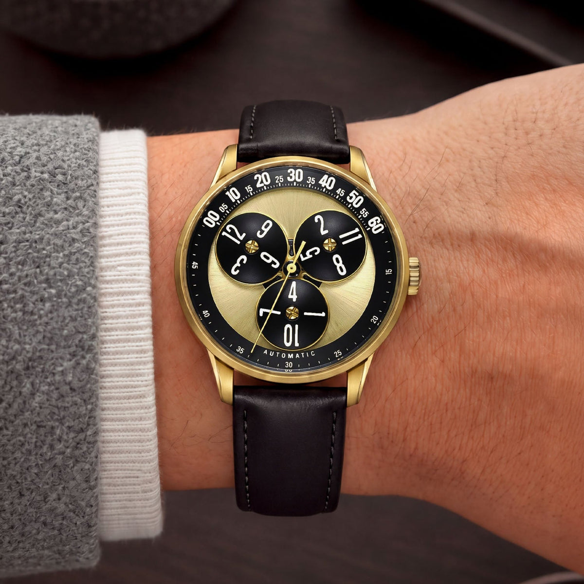 Mandetbrote Wandering Hour Gold — Worn on wrist with a grey sleeve, showing the wandering hour display, available at IFL Watches.